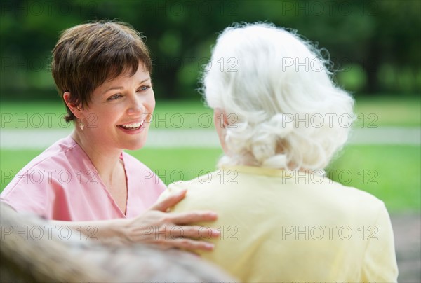 Senior woman and nursing assistant relaxing on outdoor sofa.