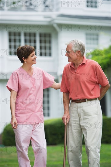 Senior man and nursing assistant walking in back yard.