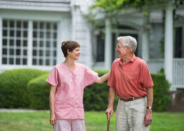 Senior man and nursing assistant walking in back yard.