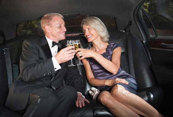 Parents of bride drinking champagne inside limousine.