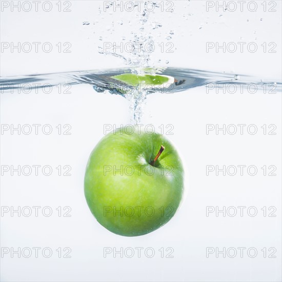 Green apple splashing into water, studio shot. Photo : Daniel Grill