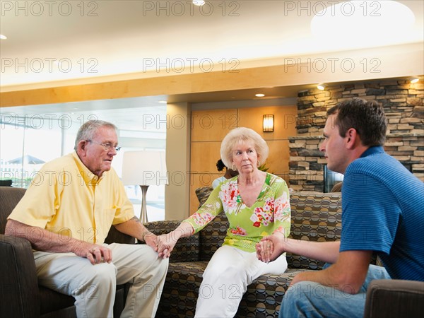 Senior people holding hands in hospital talking to doctor.