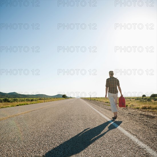 Mid adult woman carrying empty canister along empty road.