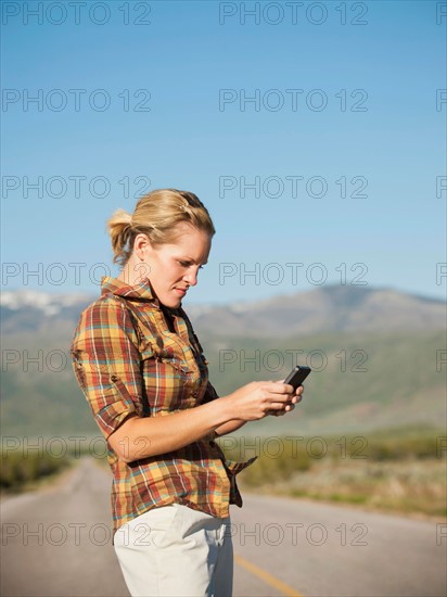 USA, Utah, Kanosh, Mid adult woman calling emergency services on empty desert road. Photo: Erik Isakson