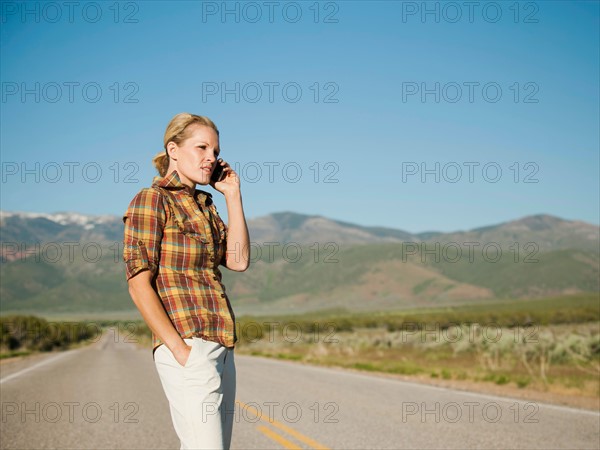 USA, Utah, Kanosh, Mid adult woman calling emergency services on empty desert road. Photo: Erik Isakson