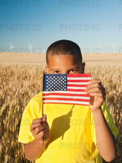 Boy (8-9) holding a small American flag in wheat field.