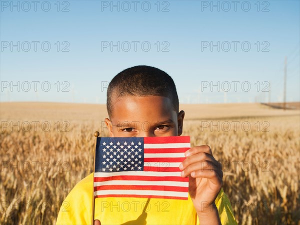 Boy (8-9) holding a small American flag in wheat field.