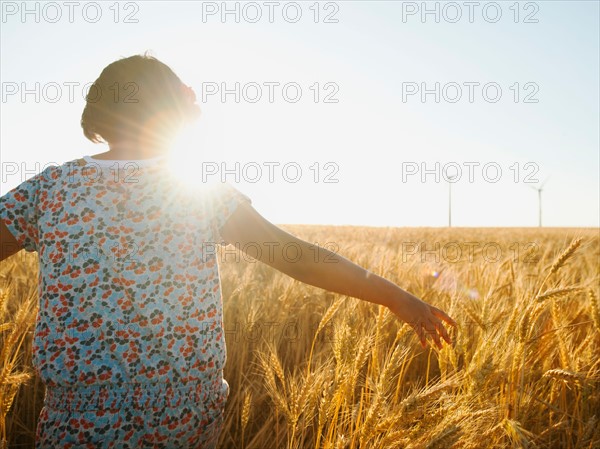 Girl (10-11) walking in glorious sunshine amidst wheat.