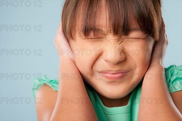 Studio shot of girl (10-11) with closed eyes covering ears. Photo : Rob Lewine