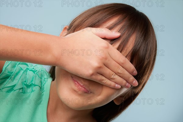 Studio shot of girl (10-11) covering eyes with hand. Photo : Rob Lewine