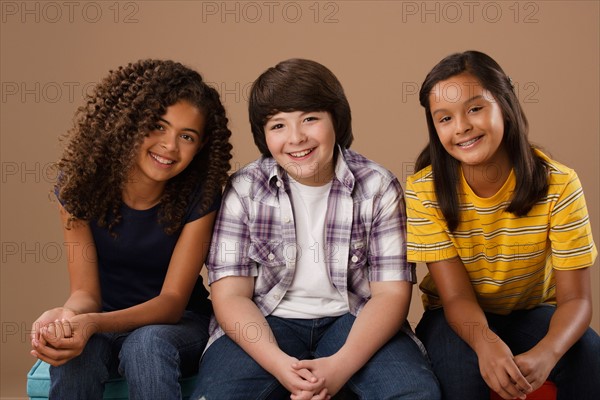 Studio portrait of boy and girls (10-11) sitting side by side. Photo: Rob Lewine
