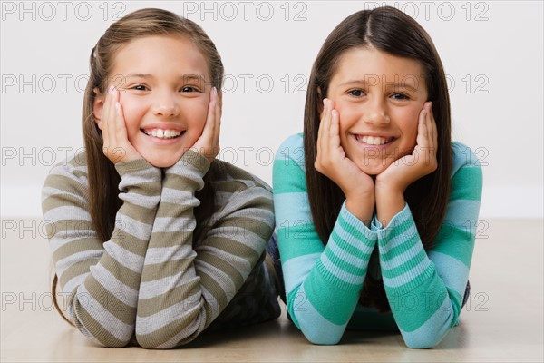 Studio portrait of two girls (8-9) lying on floor. Photo : Rob Lewine