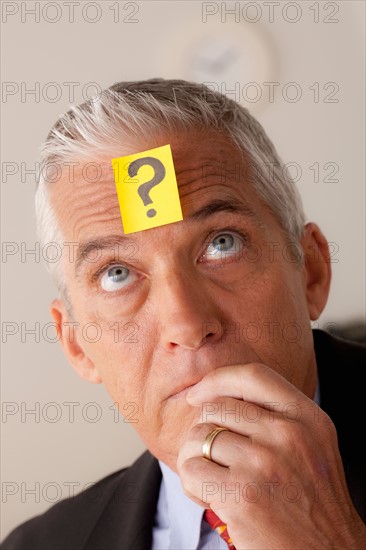 Studio portrait of senior businessman with adhesive note on forehead. Photo : Rob Lewine