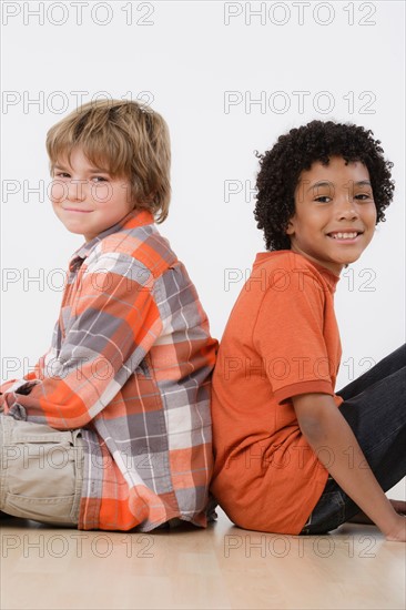 Studio portrait of two boys (8-9) sitting back to back. Photo : Rob Lewine