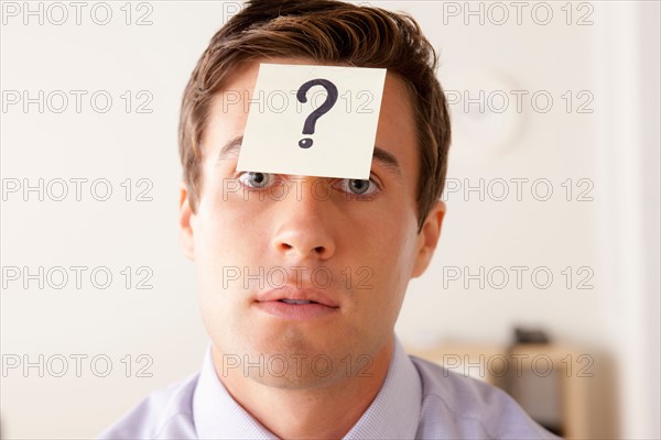 Portrait of businessman with adhesive note attached on forehead. Photo: Rob Lewine