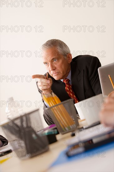 Businessman pointing finger from behind desk. Photo : Rob Lewine