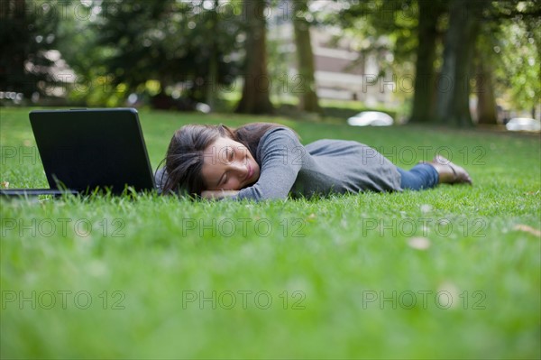 Young woman lying on grass using laptop. Photo : Jan Scherders