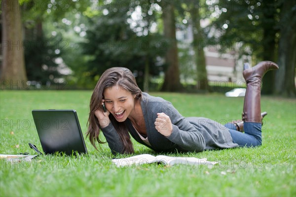 Young woman lying on grass using laptop and cell phone. Photo: Jan Scherders