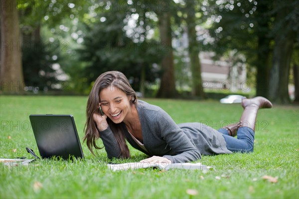 Young woman lying on grass using laptop and cell phone. Photo: Jan Scherders