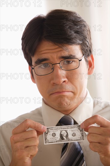 Sad business man holding one dollar note. Photo : Rob Lewine