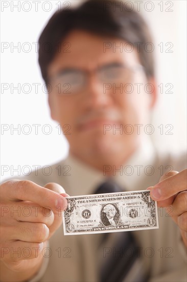 Sad business man holding one dollar note. Photo : Rob Lewine