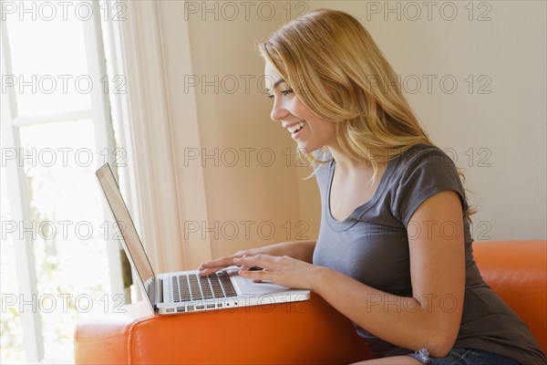 Young woman sitting on sofa using laptop. Photo: Rob Lewine