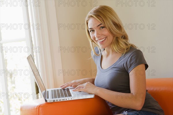 Portrait of young woman sitting on sofa using laptop. Photo: Rob Lewine