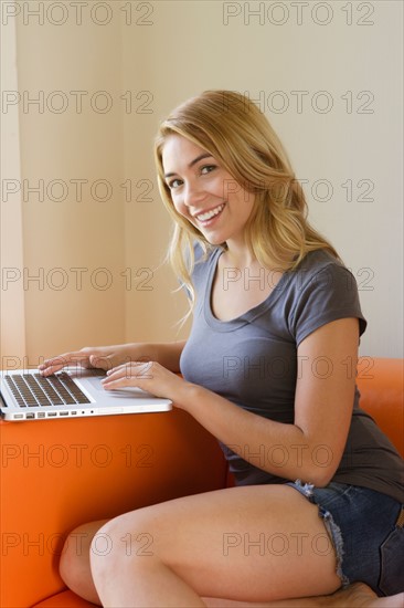 Portrait of young woman sitting on sofa using laptop. Photo: Rob Lewine