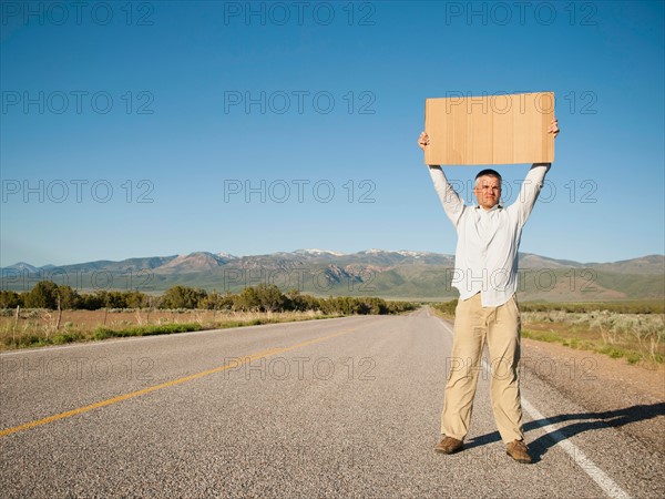 Mid-adult man hitch-hiking in barren scenery.