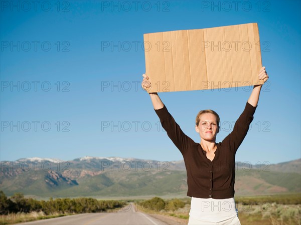 Mid-adult woman hitch-hiking in barren scenery.