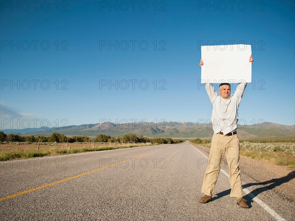 Mid-adult man hitch-hiking in barren scenery.