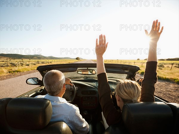 USA, Utah, Kanosh, Mad-adult couple driving through desert plains in convertible car.