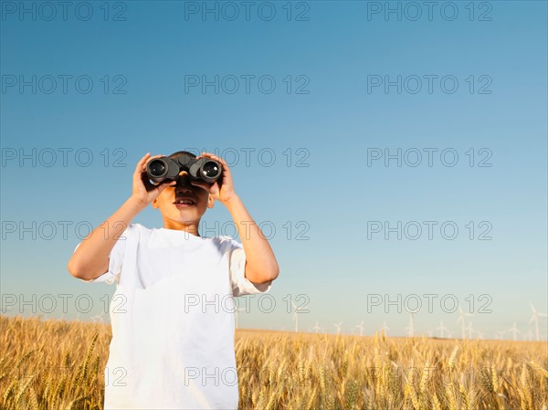Boy (8-9) standing in wheat field, looking through binoculars. Photo: Erik Isakson