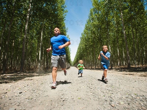 Father with sons (2-9) running down country road.
