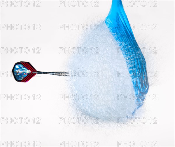 Studio shot of dart puncturing balloon filled with water.