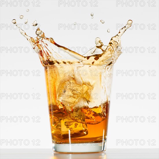 Studio shot of ice cubes splashing into glass of whiskey.