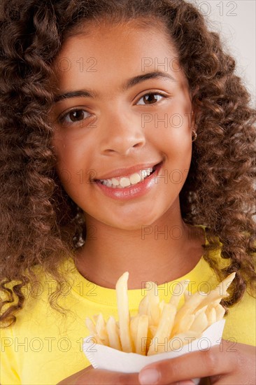 Studio portrait of girl (10-11) holding french fries. Photo : Rob Lewine