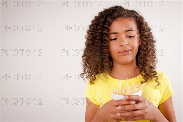 Studio portrait of girl (10-11) holding french fries. Photo : Rob Lewine