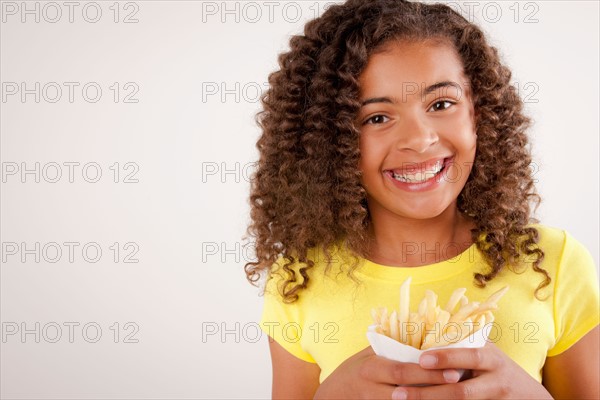 Studio portrait of girl (10-11) holding french fries. Photo : Rob Lewine