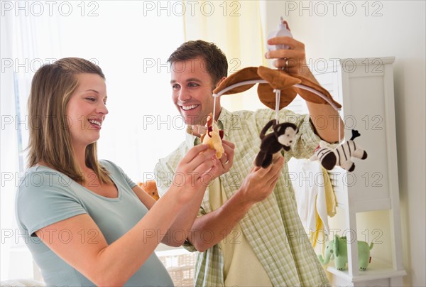 Young couple holding mobile in nursery.