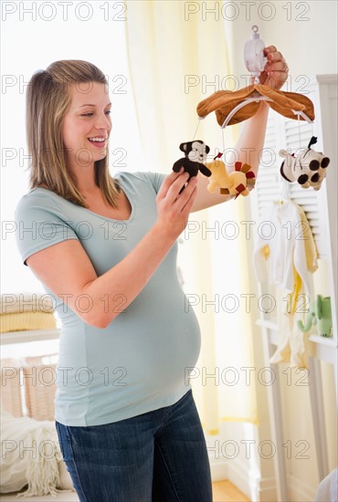 Young pregnant woman holding mobile in nursery.