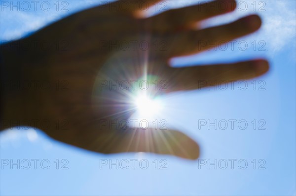 Close up of hand against blue sky with sun beams.