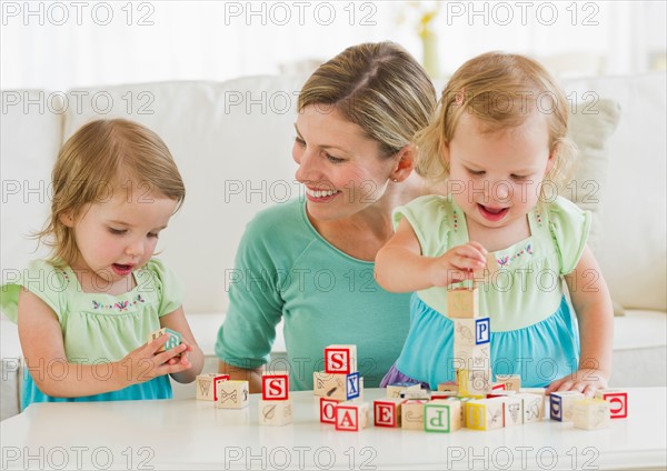 Mother and daughters (2-3) playing with letter blocks.