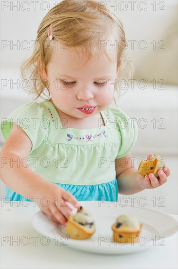 Girl (2-3) eating muffins.