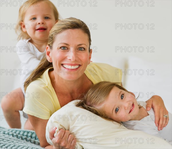 Portrait of mother with daughters (2-3) on bed.
