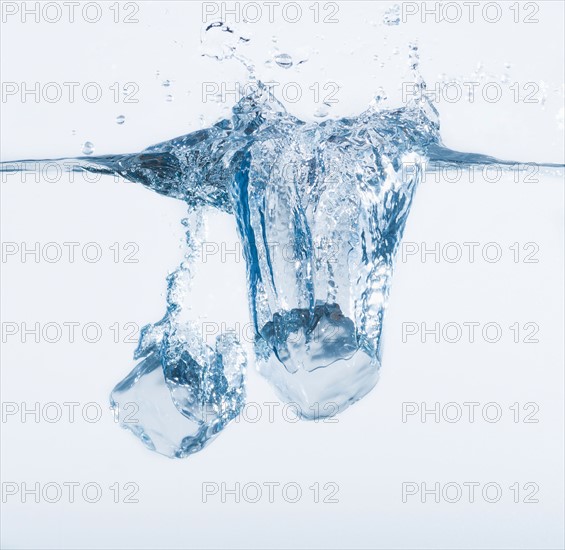 Two ice cubes splashing into water, studio shot. Photo : Daniel Grill