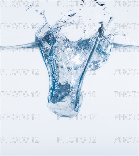 Ice cube splashing into water, studio shot. Photo : Daniel Grill