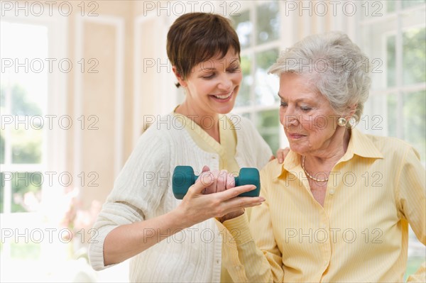 Senior woman lifting dumbbell, nurse assisting her.