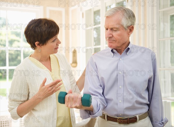 Senior man lifting dumbbell, nurse assisting him.