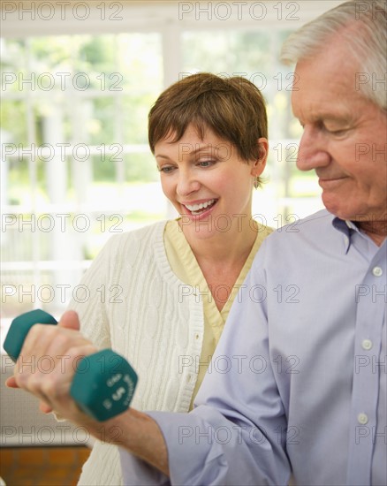 Senior man lifting dumbbell, nurse assisting him.